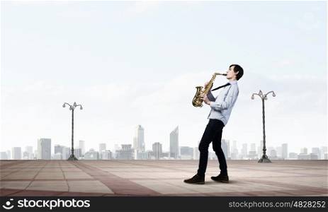 Handsome saxophonist. Young man walking in city and playing saxophone