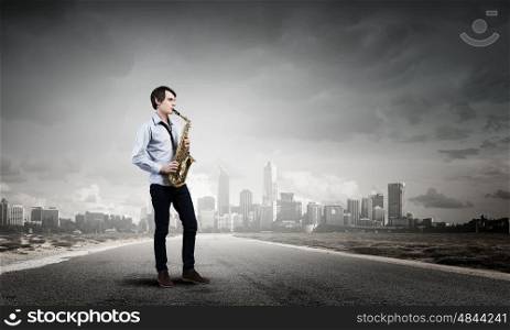 Handsome saxophonist. Young man walking on road playing saxophone