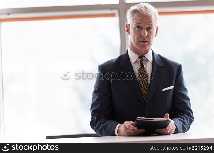 handsome senior business man with grey hair working on tablet computer at modern bright office interior