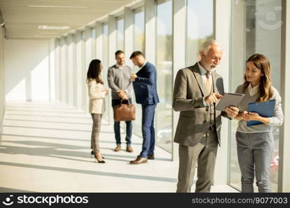 Handsome senior business man with his young female coleague using digital tablet in the office