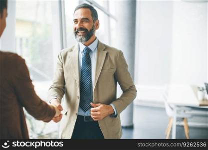 Handsome senior businessman handshaking with young woman in the office