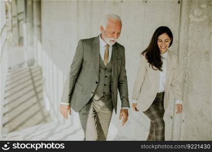 Handsome senior corporate business professional and his young female colleague climbing at stairs in office corridor