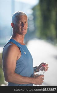 handsome senior jogging man drinking fresh water from bottle after mornig run