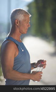 handsome senior jogging man drinking fresh water from bottle after mornig run