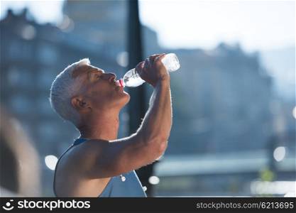 handsome senior jogging man drinking fresh water from bottle after mornig run