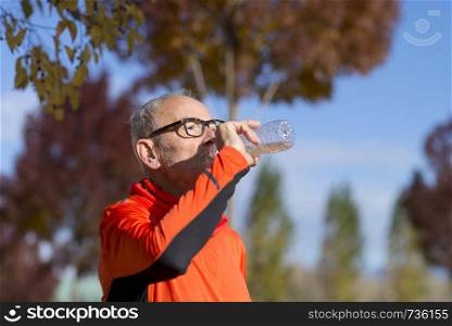Handsome senior jogging man drinking fresh water from bottle after morning run