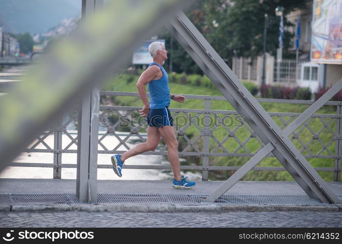 handsome senior man athlete jogging and have morning workout with sunrise and city in background