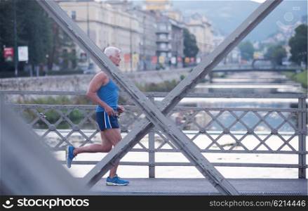 handsome senior man athlete jogging and have morning workout with sunrise and city in background