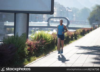 handsome senior man athlete jogging and have morning workout with sunrise and city in background