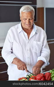 Handsome senior man cooking at home preparing salad in kitchen.