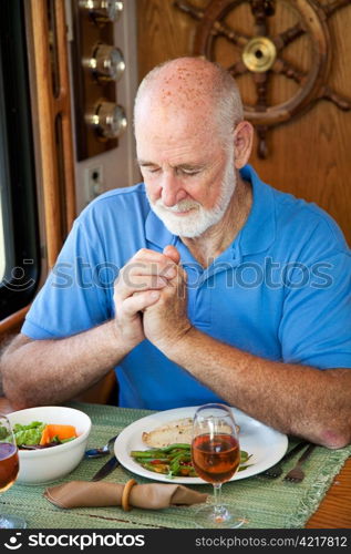 Handsome senior man saying grace over a meal in his motor home.