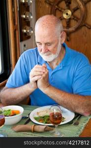 Handsome senior man saying grace over a meal in his motor home.