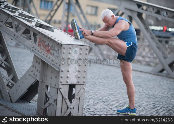 handsome senior man stretching and warming up before jogging exercise at early mornig