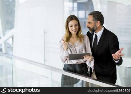Handsome smiling mature businessman and his cute young female coworker with digital tablet in the modern office