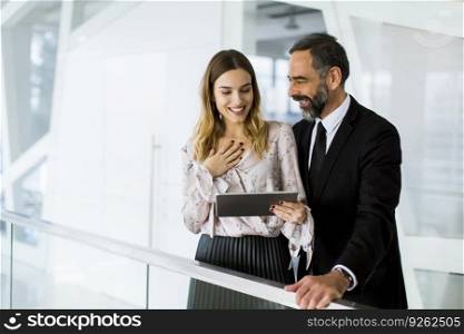 Handsome smiling mature businessman and his cute young female coworker with digital tablet in the modern office