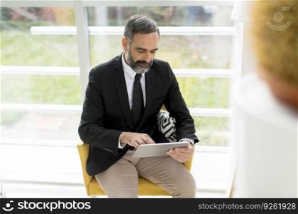 Handsome smiling mature businessman with digital tablet in the office working, reading or searching something