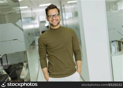 Handsome smiling young businessman in glasses standing in the modern office