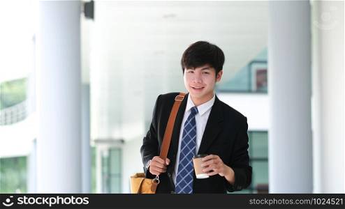 Handsome smiling young businessman wearing suit walking outdoor holding coffee cup while coffee break.