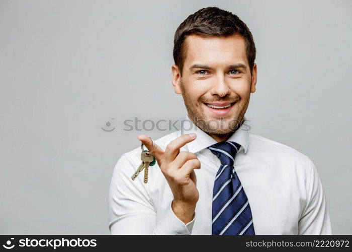 Handsome stylish caucasian businessman holding keys on grey background with copy space. Handsome stylish businessman on grey background