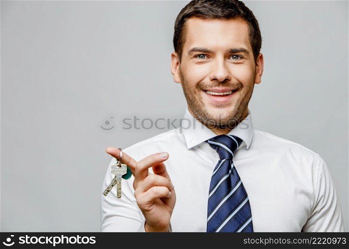 Handsome stylish caucasian businessman holding keys on grey background with copy space. Handsome stylish businessman on grey background