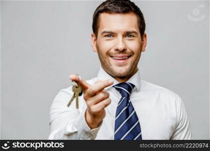 Handsome stylish caucasian businessman holding keys on grey background with copy space. Handsome stylish businessman on grey background