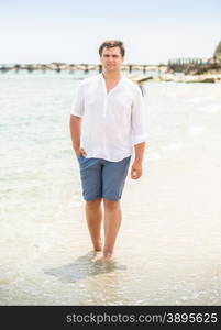 Handsome stylish man in white shirt walking on the seashore