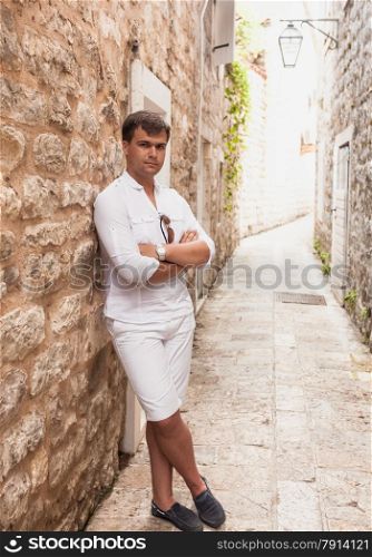 Handsome stylish man leaning against old stone wall on street