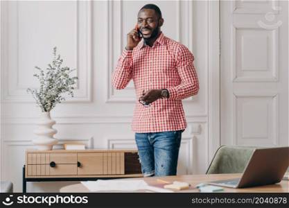 Handsome successful young african businessman in casual clothes enjoying phone call, using modern smartphone at work, smiling afro american guy office worker consulting client via mobile in office. Handsome successful young african businessman in casual clothes enjoying phone call, usingsmartphone