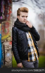 handsome trendy man outdoor in city setting, male model wearing black jacket scarf and checked shirt against colorful graffiti wall