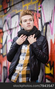 handsome trendy man outdoor in city setting, male model wearing black jacket scarf and checked shirt against colorful graffiti wall