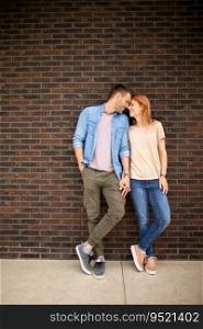 Handsome ymiling young couple in love in front of house brick wall