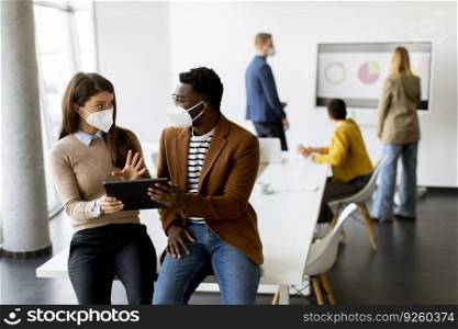 Handsome young African American business man and cute business woman working on digital tablet while wearing a facial protective masks