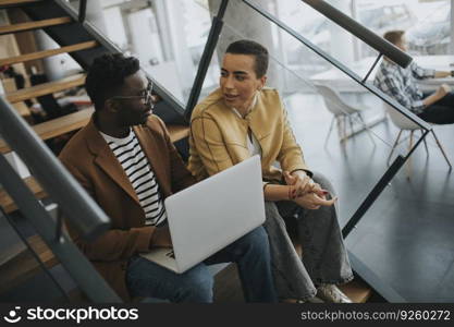 Handsome young African American business man and short hair woman working on laptop while sitting at office stairs