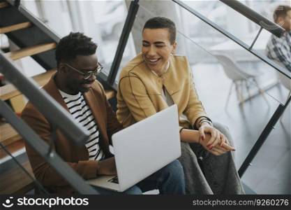 Handsome young African American business man and short hair woman working on laptop while sitting at office stairs