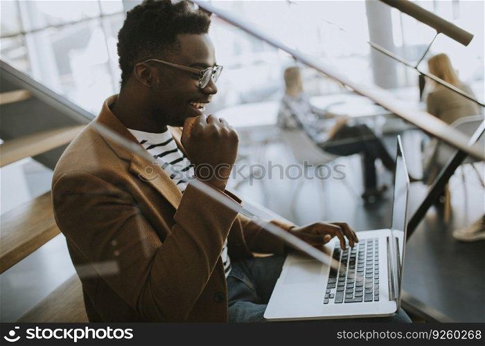 Handsome young African American business man working on laptop computer while sitting on a office stairs