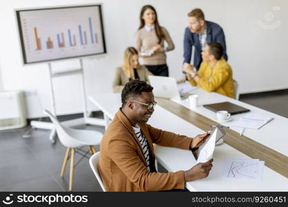 Handsome young African American business man working with digital tablet in front of his coworkers at boardroom