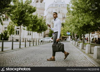 Handsome young African American businessman using a mobile phone while ceossing a street