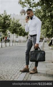 Handsome young African American businessman using a mobile phone while waitng for a taxi on a street