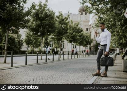 Handsome young African American businessman using a mobile phone while waitng for a taxi on a street