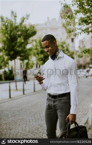 Handsome young African American businessman using a mobile phone while waitng for a taxi waitng a taxi on a street