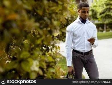 Handsome young African American businessman using a mobile phone while walking on a street