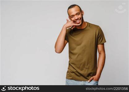 Handsome young African American man showing a call me sign and smiling while standing isolated on grey background.. Handsome young African American man showing a call me sign and smiling while standing isolated on grey background