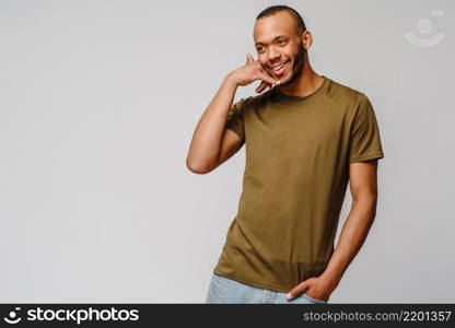 Handsome young African American man showing a call me sign and smiling while standing isolated on grey background.. Handsome young African American man showing a call me sign and smiling while standing isolated on grey background