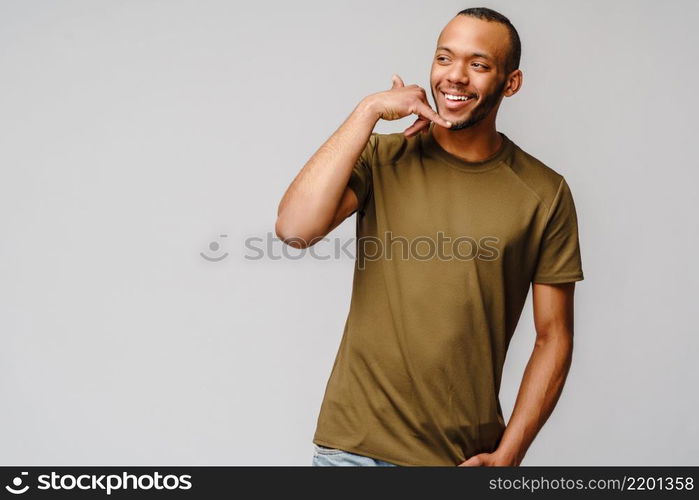 Handsome young African American man showing a call me sign and smiling while standing isolated on grey background.. Handsome young African American man showing a call me sign and smiling while standing isolated on grey background