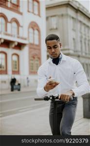 Handsome young African American using mobile phone while standing with electric scooter on a street
