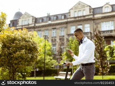 Handsome young African American using mobile phone while standing with electric scooter on a street