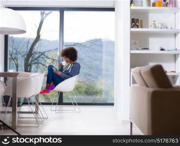 Handsome young african american woman drinking coffee and using a mobile phone at home