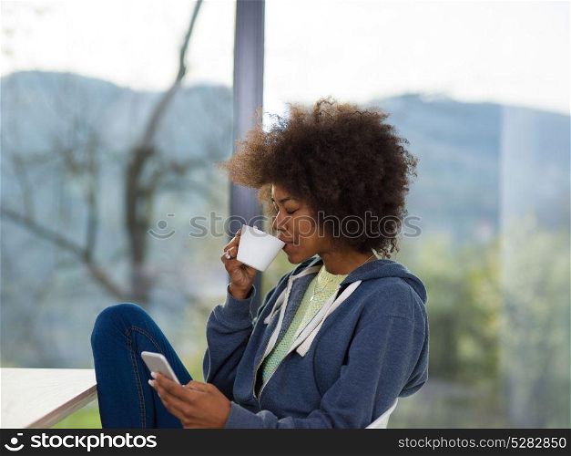 Handsome young african american woman drinking coffee and using a mobile phone at home
