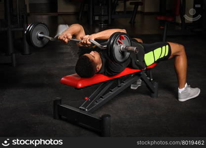 handsome young african descent mixed race man doing bench french press workout with barbell in gym. Young man doing arms bench french press workout in gym