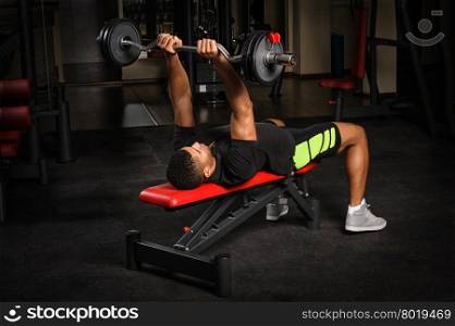 handsome young african descent mixed race man doing bench french press workout with barbell in gym. Young man doing arms bench french press workout in gym